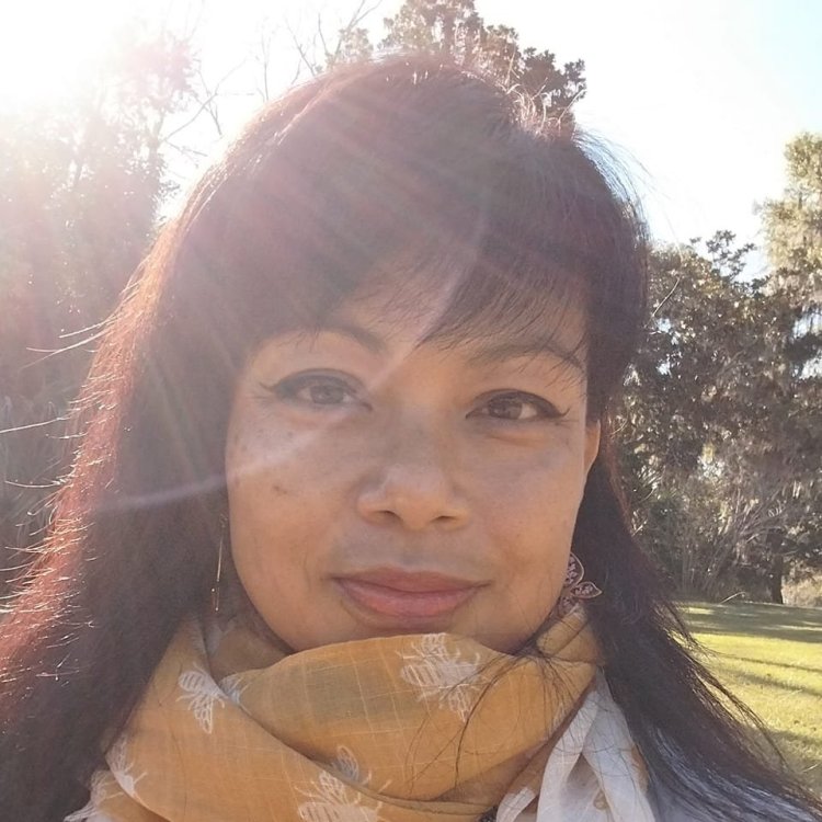 Genevieve Cheung bathed in sunlight, wearing a golden scarf, smiling softly.