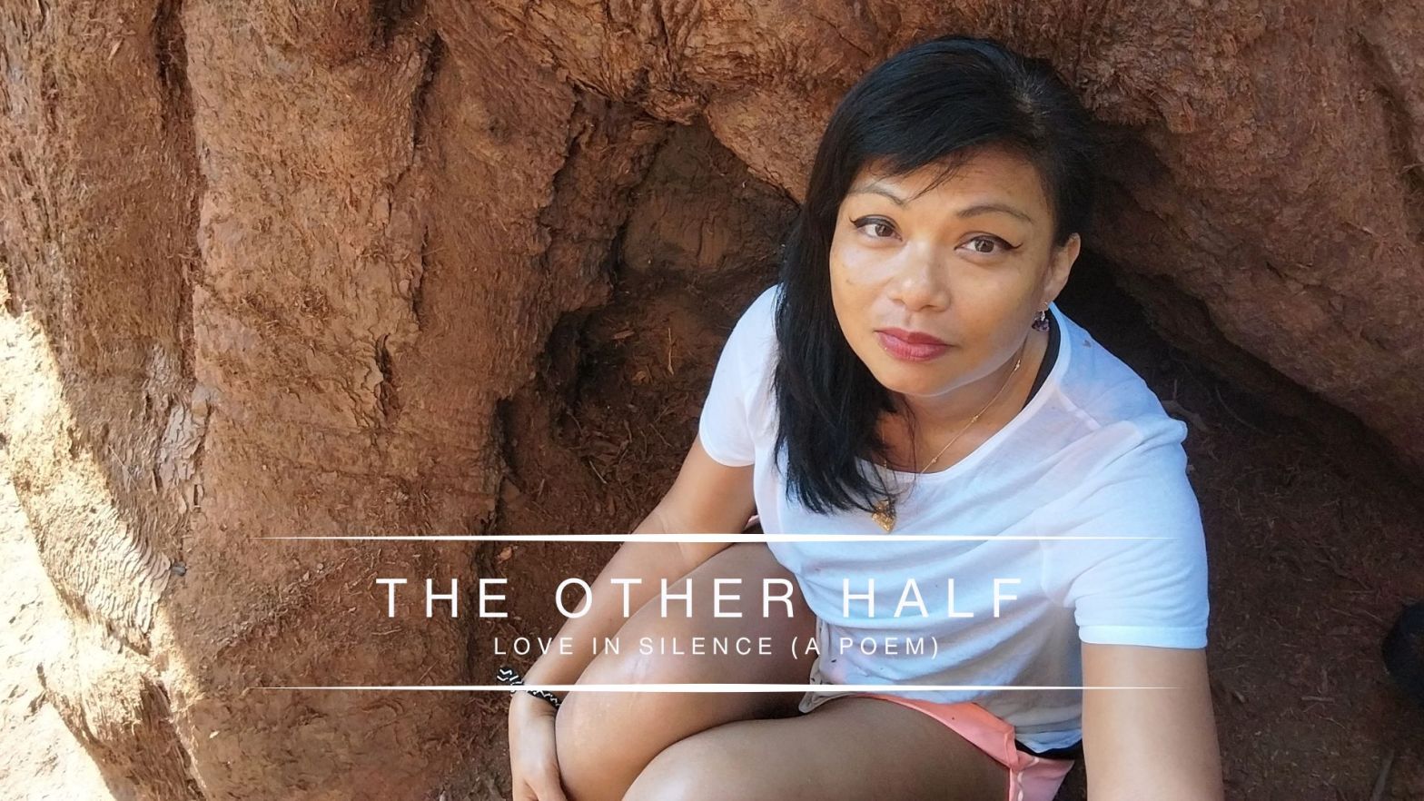 Genevieve Cheung sitting quietly inside a natural rock formation, looking directly at the camera, reflecting on love, silence, and inner wholeness.