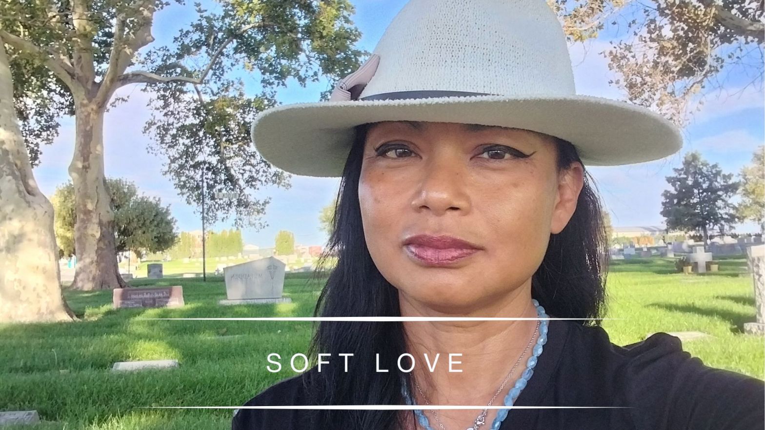 Genevieve Cheung wearing a light hat standing in a peaceful cemetery with trees and soft sunlight, reflecting on soft love and saudade.